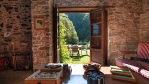 A stone-walled room with a wooden table, a red-striped sofa, and a view of a garden through an open door. - Fantastic family villa with pool.... (Barga)