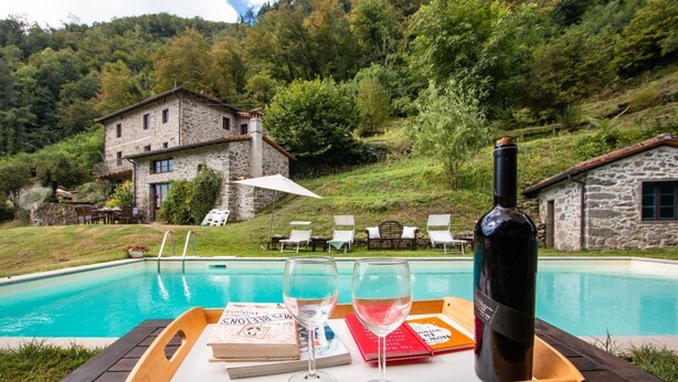 A poolside setting with a wooden table, two wine glasses, a bottle of wine, and books. - Fantastic family villa with pool.... (Barga)
