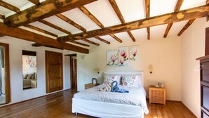 A bedroom with wooden beams, a bed with floral bedding, a nightstand, and a wall with floral paintings. - Fantastic family villa with pool.... (Barga)