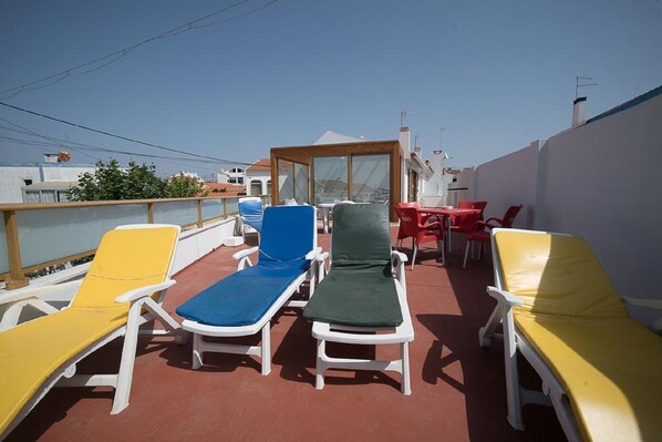 Eine Dachterrasse mit weißen Liegestühlen und einem Tisch, die einen Blick auf die umliegenden Gebäude bietet.