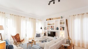 A modern living room with a sofa, armchair, coffee table, bookshelf, and a TV.