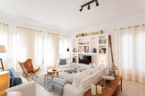 A modern living room with a sofa, armchair, coffee table, bookshelf, and a TV. - On The Rocks - The Main House - Serviced Villa (Ios)