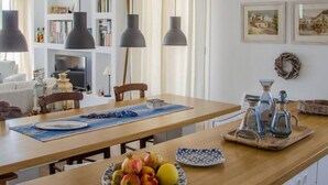A modern kitchen with pendant lights, a wooden island with fruit, a coffee station, and a bookshelf.