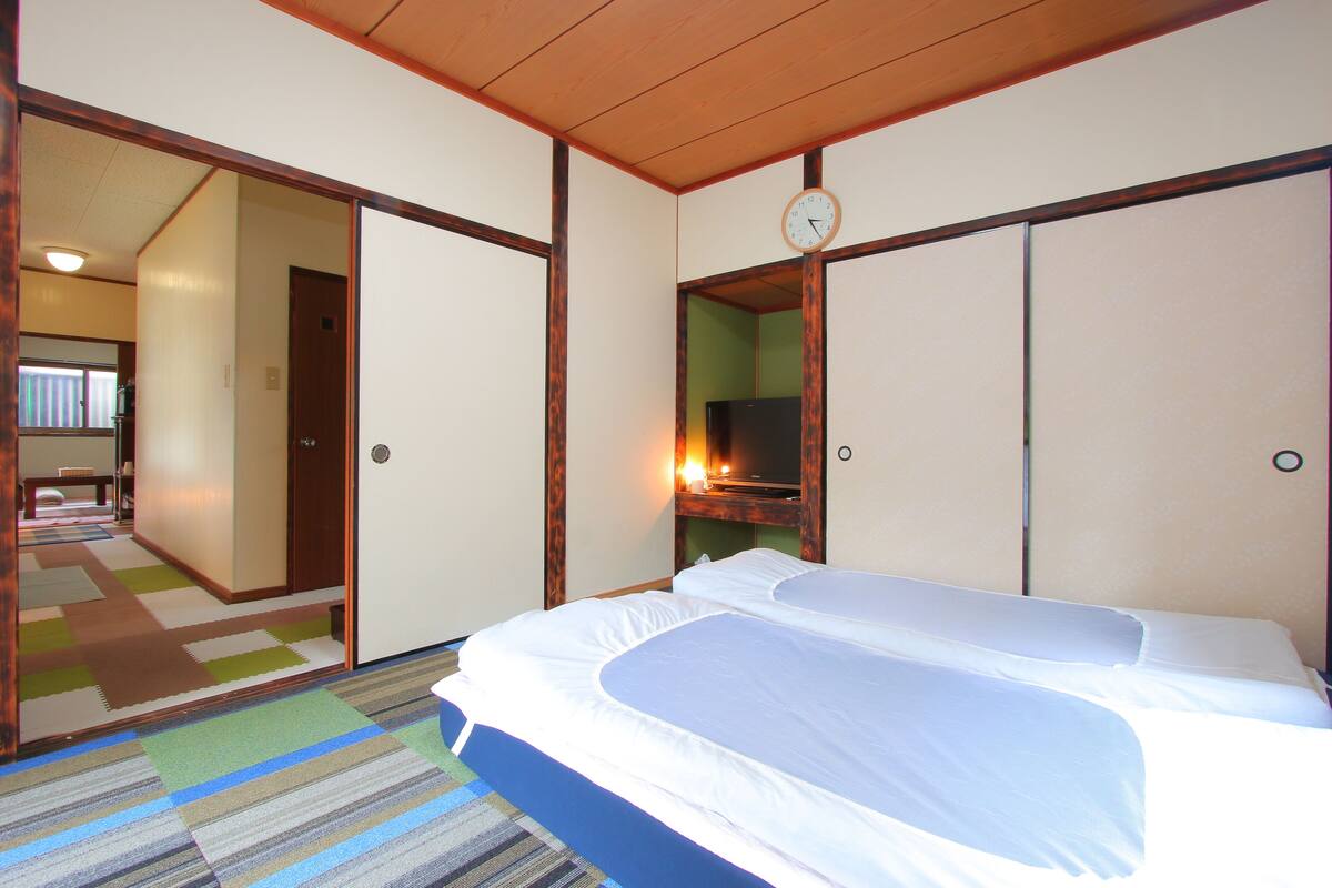 Habitación de hotel con una cama, un reloj y vistas a un pasillo con una mesa y sillas.