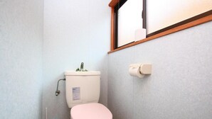 A small bathroom with a white toilet, a pink seat, a window, and a toilet paper holder. - Senju no sato Ramune Onsen (Kirishima)