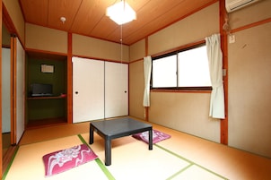 Una habitación tradicional japonesa con suelo de tatami, una mesa baja, puertas correderas y un ventanal con cortinas.