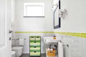 Un baño con lavamanos blanco, un espejo, toallero y ventana.