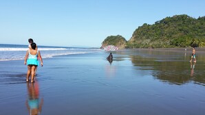Une plage avec un ciel dégagé, une mer calme et une personne qui se promène.