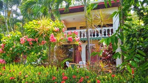 Un jardin tropical avec un kiosque blanc, des fleurs rouges et différentes plantes vertes.