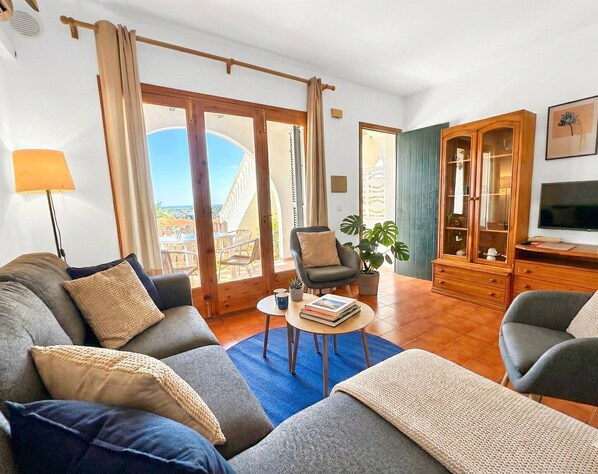 A living room with a sofa, armchairs, a coffee table, a TV, and a view of the outside.
