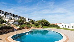 Una piscina de borde curvo, un muro de piedra y una escalera que conduce a un edificio blanco con balcones.