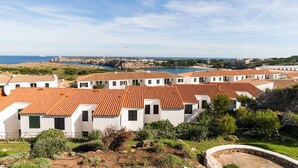 Una zona costera con edificios blancos y tejados rojos, cielo despejado y vista al mar.
