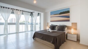 Een slaapkamer met een groot bed, een nachtkastje met een lamp, en een schilderij van een strandzicht aan de muur.