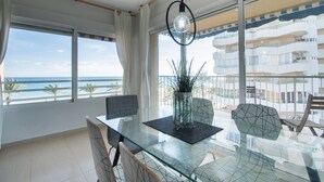 Een moderne eethoek met een glazen tafel, metalen stoelen en uitzicht op de oceaan door grote ramen.