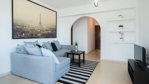 Een moderne woonkamer met een modulaire bank, een flatscreen televisie, een stadsgezicht in een lijst en een minimalistische wandplank.