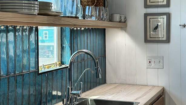 A kitchen with a wooden countertop, stainless steel sink, and a window with a view. There are shelves with dishes and glasses, and a woven basket. - Surfside Beach, Texas. Fantastic views of the beach and bay. Steps to the beach (Freeport)