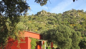 A red building with a garden in front, surrounded by trees and hills. - Charming spacious barn in beautiful tranquil scenery, pool on property (Albalá del Caudillo)