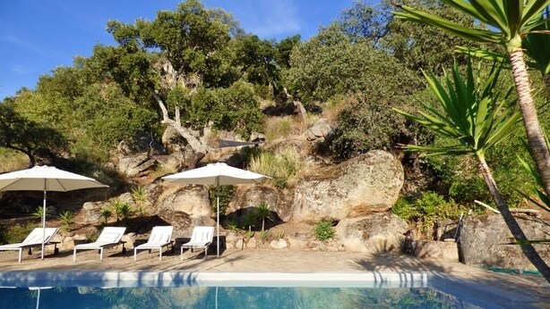 A pool area with lounge chairs and umbrellas, surrounded by rocks and trees. - Charming spacious barn in beautiful tranquil scenery, pool on property (Albalá del Caudillo)
