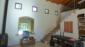 A spacious living room with a wooden ceiling, a fireplace, a staircase, and a bookshelf. - Charming spacious barn in beautiful tranquil scenery, pool on property (Albalá del Caudillo)
