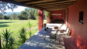 An outdoor patio with a table and chairs, a red wall, and a view of a grassy field. - Charming spacious barn in beautiful tranquil scenery, pool on property (Albalá del Caudillo)