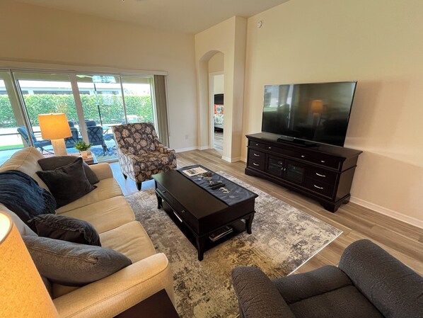 A living room with a sofa, armchairs, a coffee table, a TV, and a lamp.