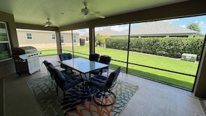 Une terrasse avec une table et des chaises, un barbecue et un ventilateur de plafond.