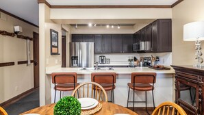 Una cocina moderna con armarios oscuros, una isla central y un comedor con sillas de madera y una mesa.