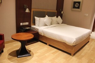 Habitación de hotel con una cama de madera, ropa de cama blanca, una mesa redonda de madera y una silla roja.
