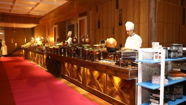 A long counter with chefs preparing food, surrounded by shelves with kitchen items. - The Utsav Grand Banquets & Resort (Sonepat)