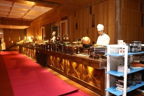 A long counter with chefs preparing food, surrounded by shelves with kitchen items. - The Utsav Grand Banquets & Resort (Sonepat)