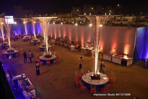 Un espacio para eventos al aire libre con mesas redondas, sillas y una zona de escenario.