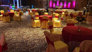 Un salón de banquetes con mesas redondas cubiertas con manteles rojos, sillas con cintas amarillas y una alfombra estampada.