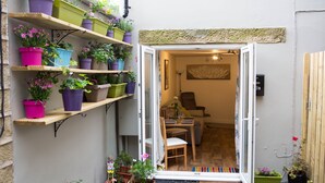 Un espacio habitable pequeño y abierto, con una mesa y sillas de madera, un sofá y varios maceteros con plantas en estantes y el suelo.