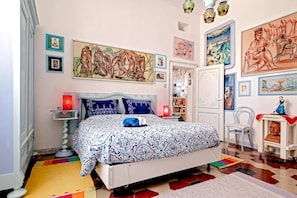A bedroom with a large bed, a bedside table, a chair, and a bookshelf.