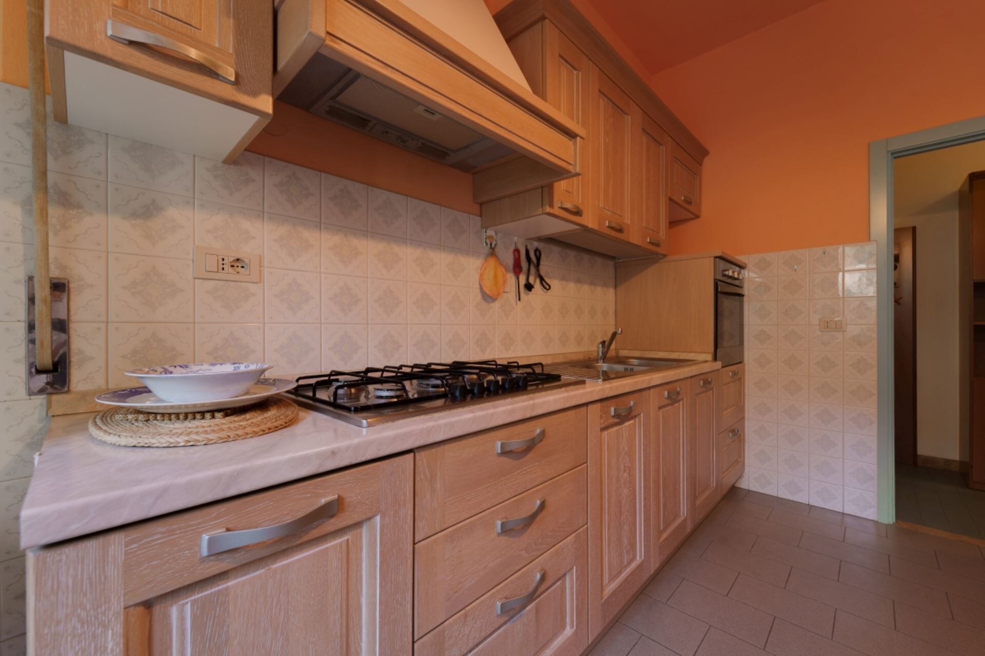 Una cocina con armarios de madera, una estufa a gas, un lavamanos y un salpicadero de azulejos.