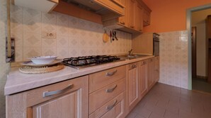Eine Küche mit Holzschränken, einem Gasherd, einer Spüle und einer gefliesten Rückwand.