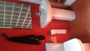 A bathroom with a red tiled floor, a white sink, a toilet, and a black jacket hanging on the wall. - central sun loft- door of the sun (MADRID)