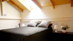 A bedroom with a bed, two bedside lamps, a nightstand, a vase with flowers, and a wooden ceiling. - central sun loft- door of the sun (MADRID)