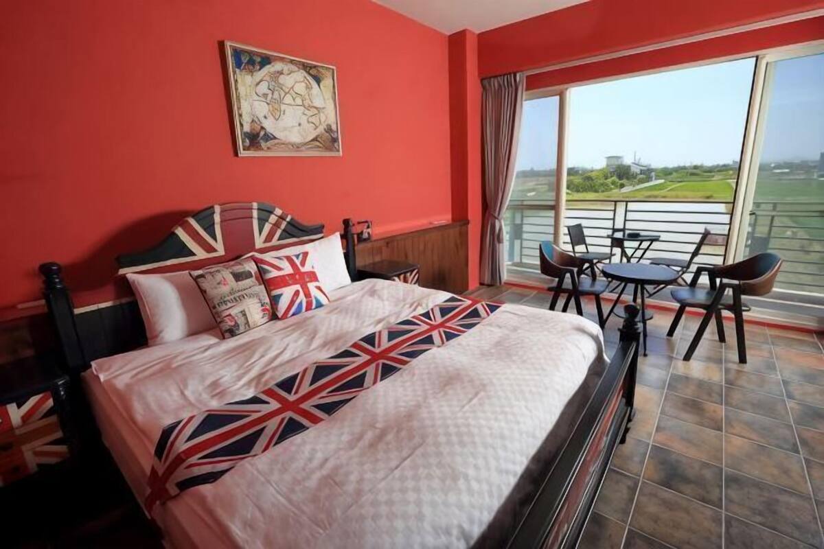 A hotel room with a large bed, a balcony with a table and chairs, and a view of the landscape.
