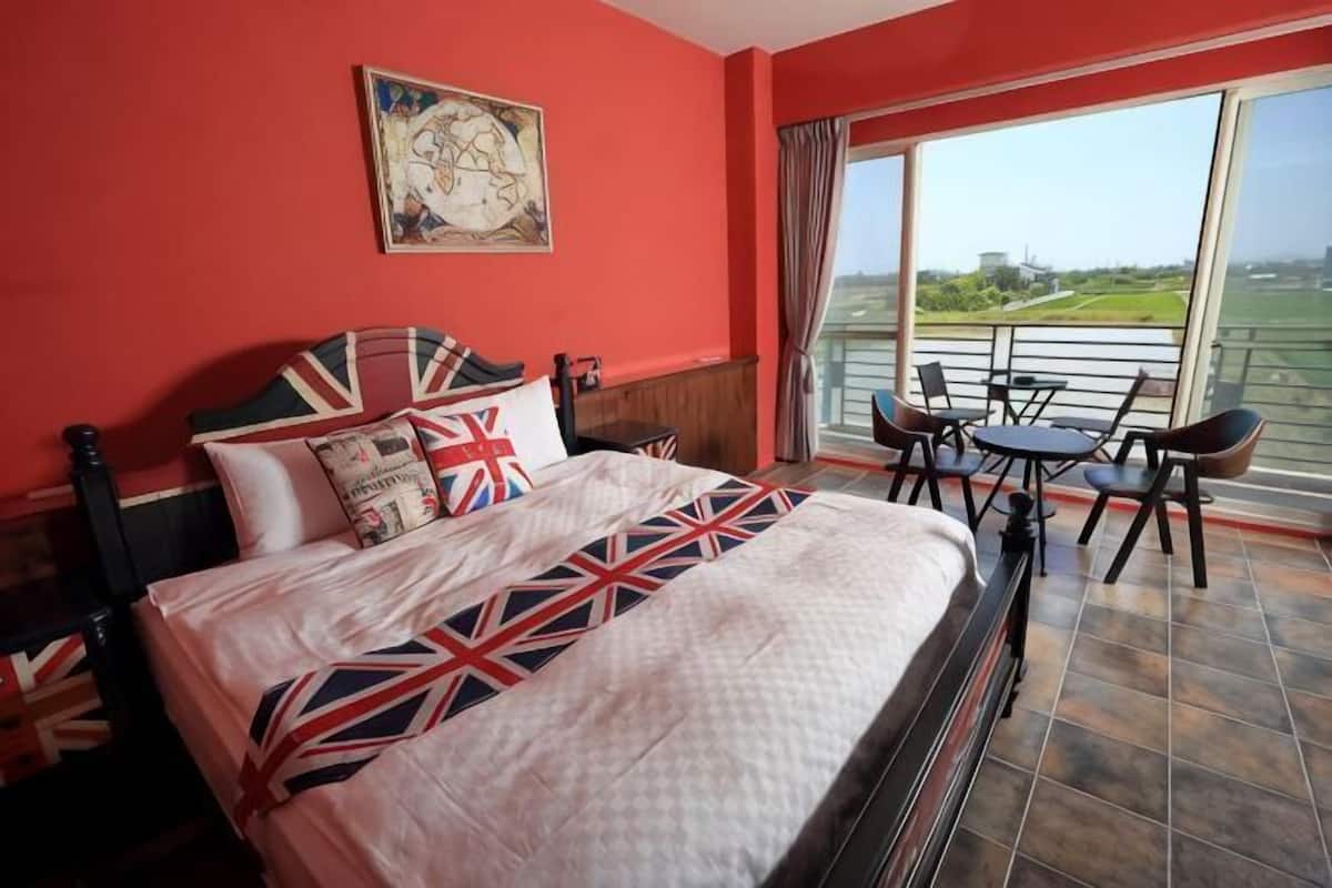 Quarto de hotel com uma cama grande, varanda com mesa e cadeiras, e vista para a paisagem.