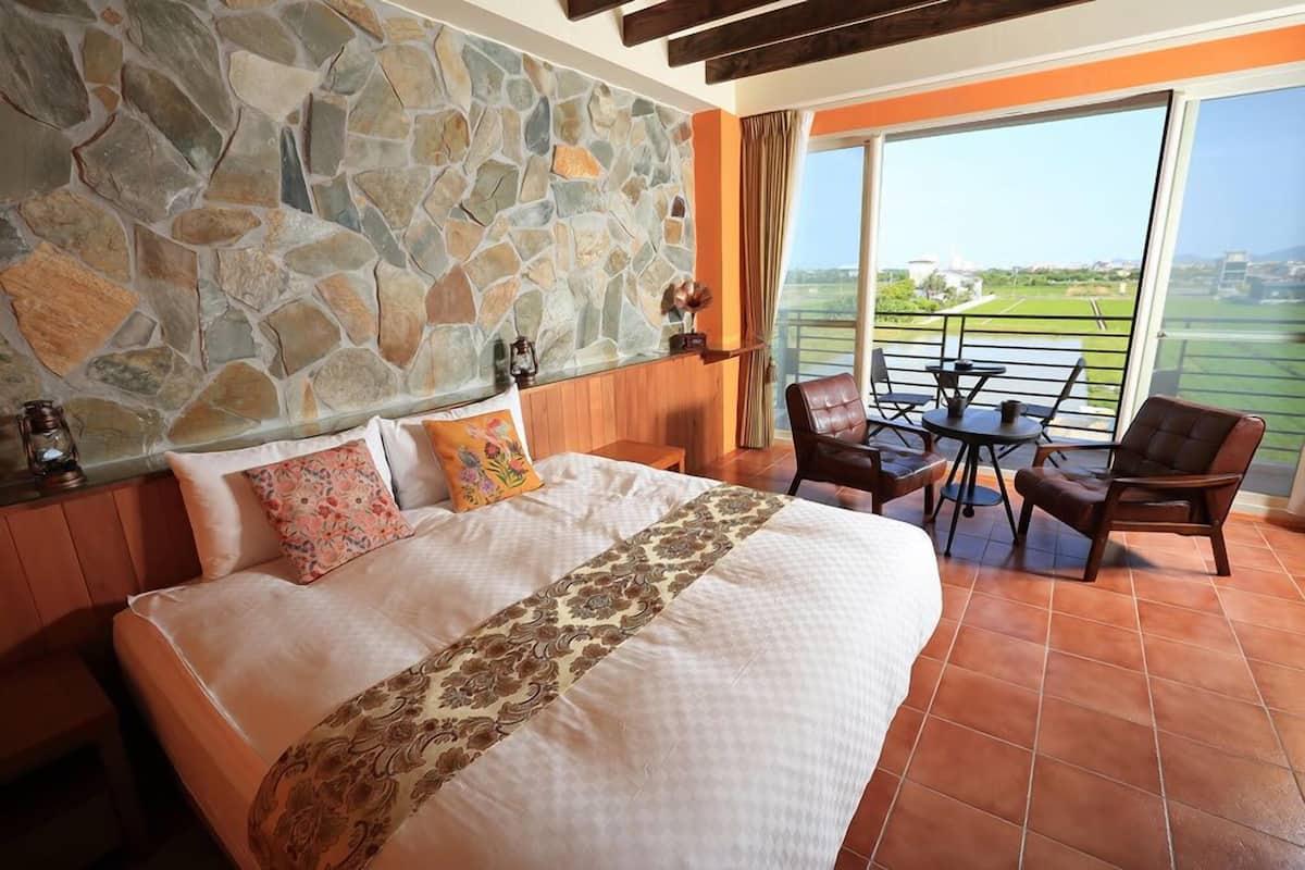 A bedroom with a large bed, stone wall, and a balcony with a table and chairs.