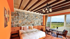 A bedroom with a stone wall, wooden ceiling beams, a large bed, a balcony with a view, and a dining area. - Green Resort (Wujie)