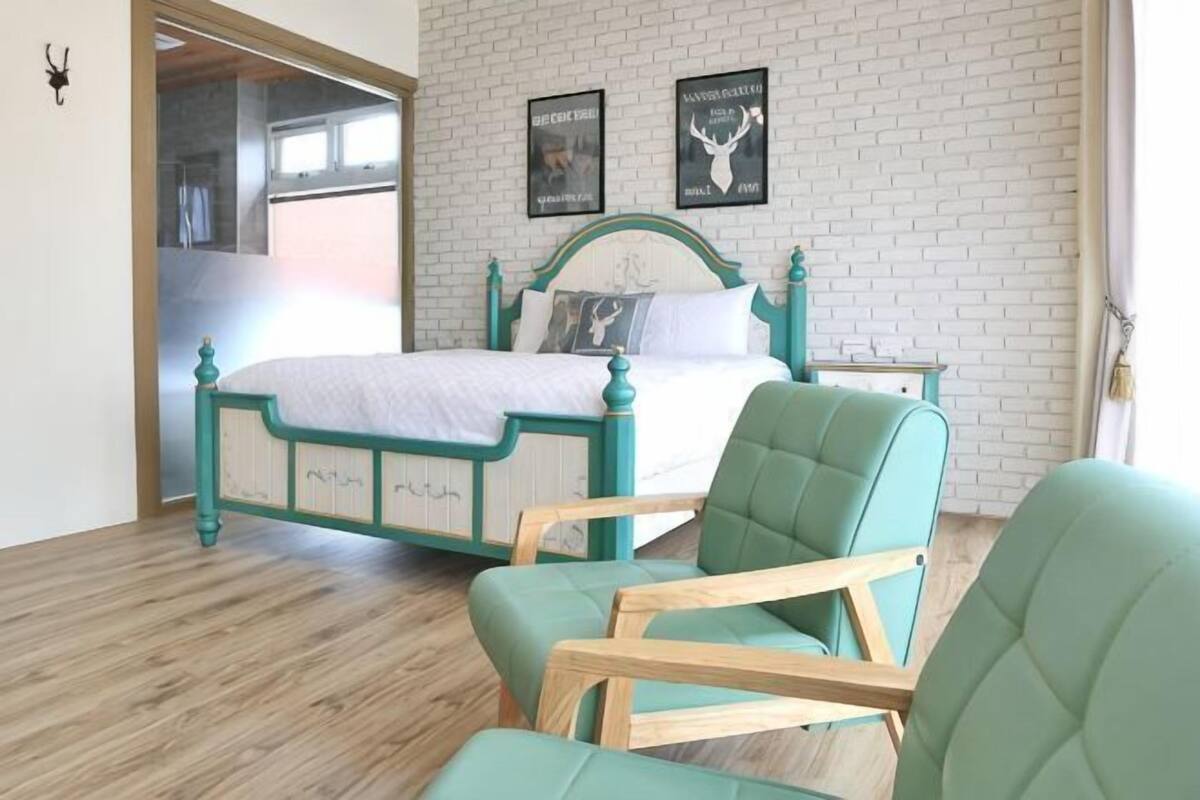 A bedroom with a bed, a chair, a nightstand, and a brick wall with two posters.