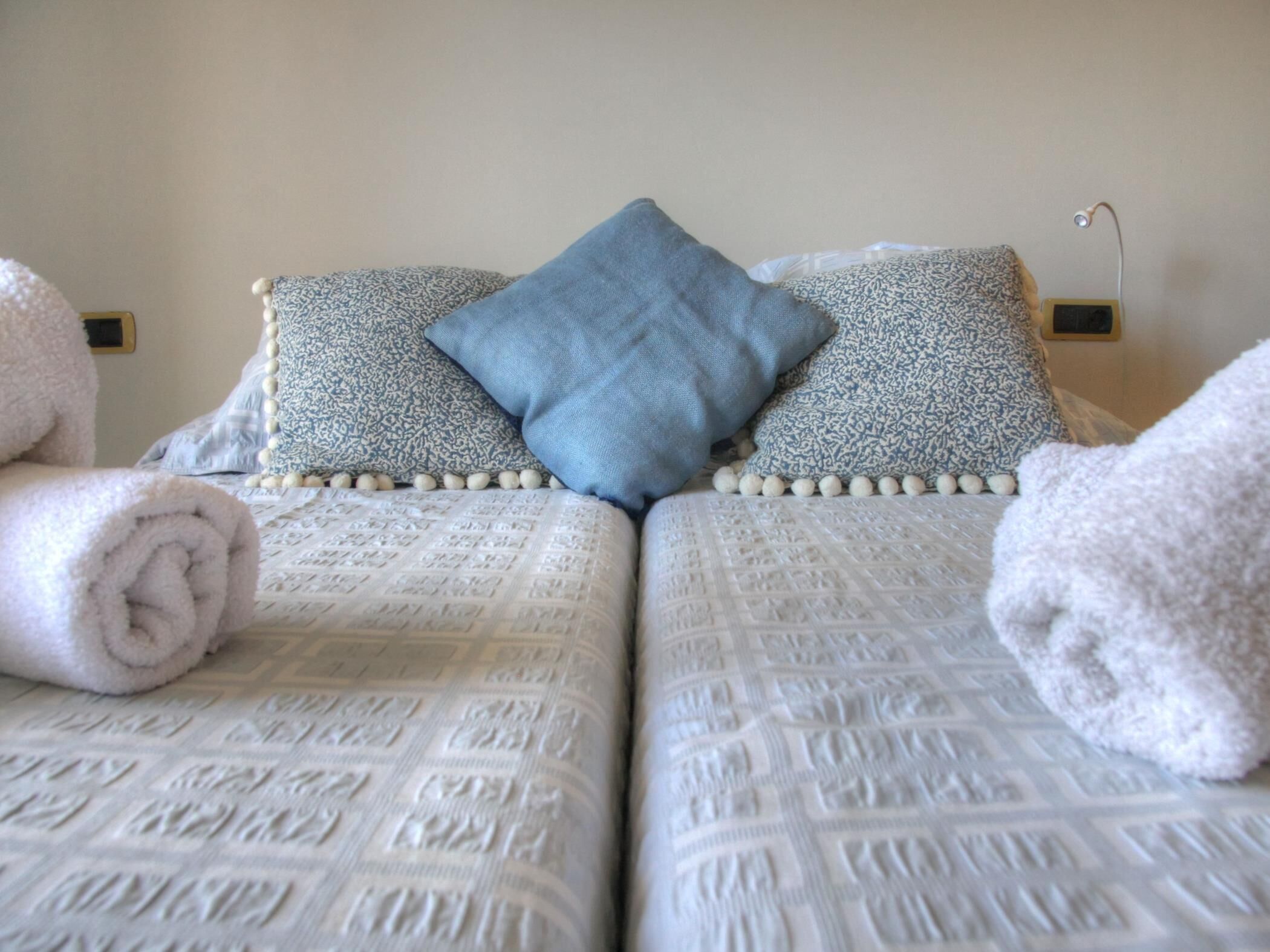 A neatly made bed with patterned bedding, two pillows, and rolled towels.