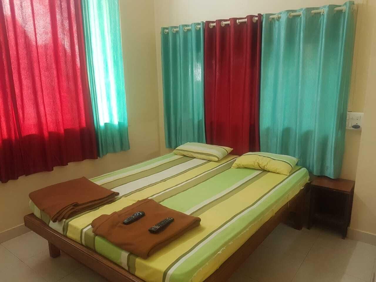 A single bed with striped bedding, a nightstand, and two remote controls on the bed.