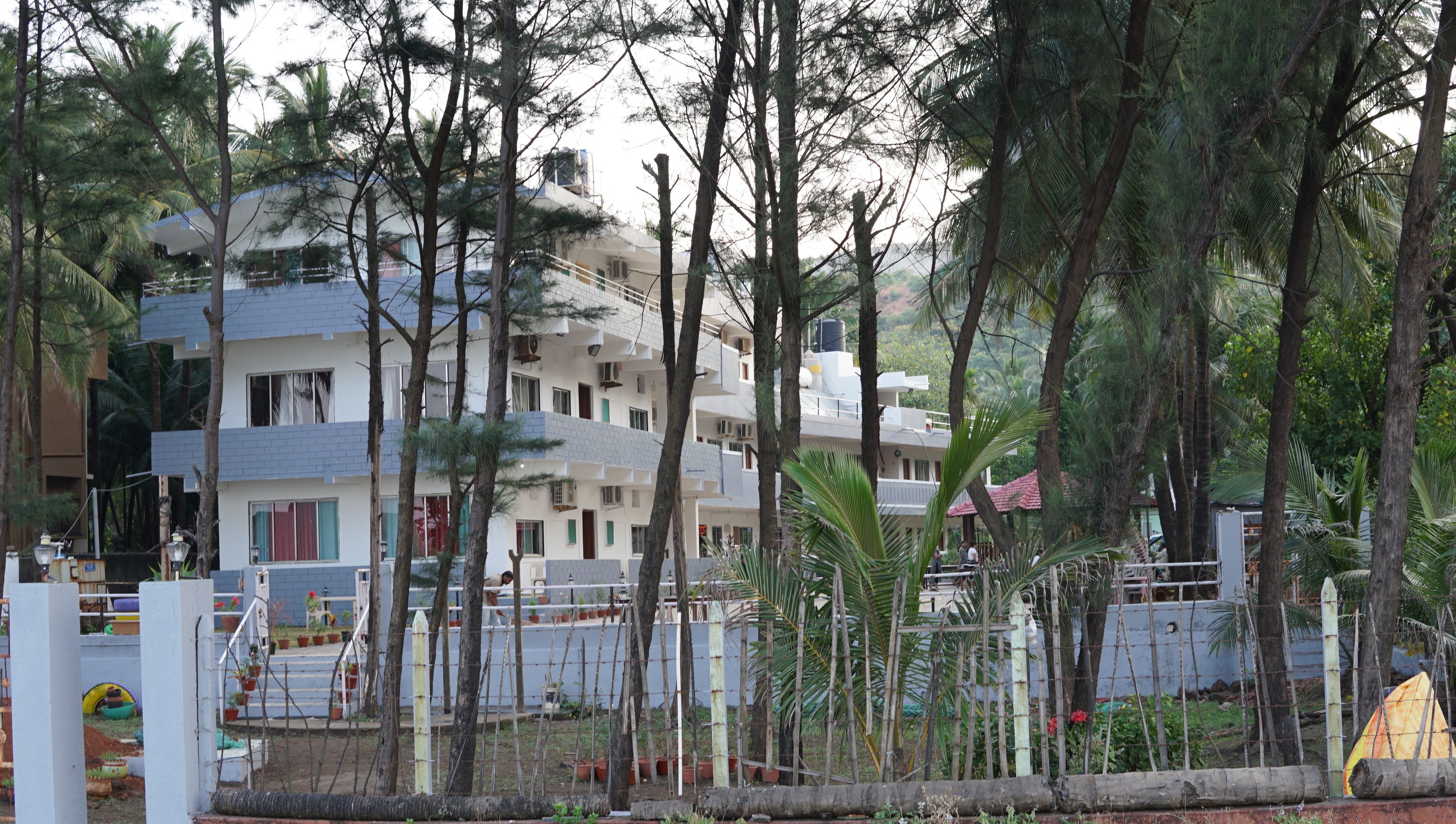 Un edificio residencial de varios pisos con balcones, rodeado de árboles y un jardín cercado.