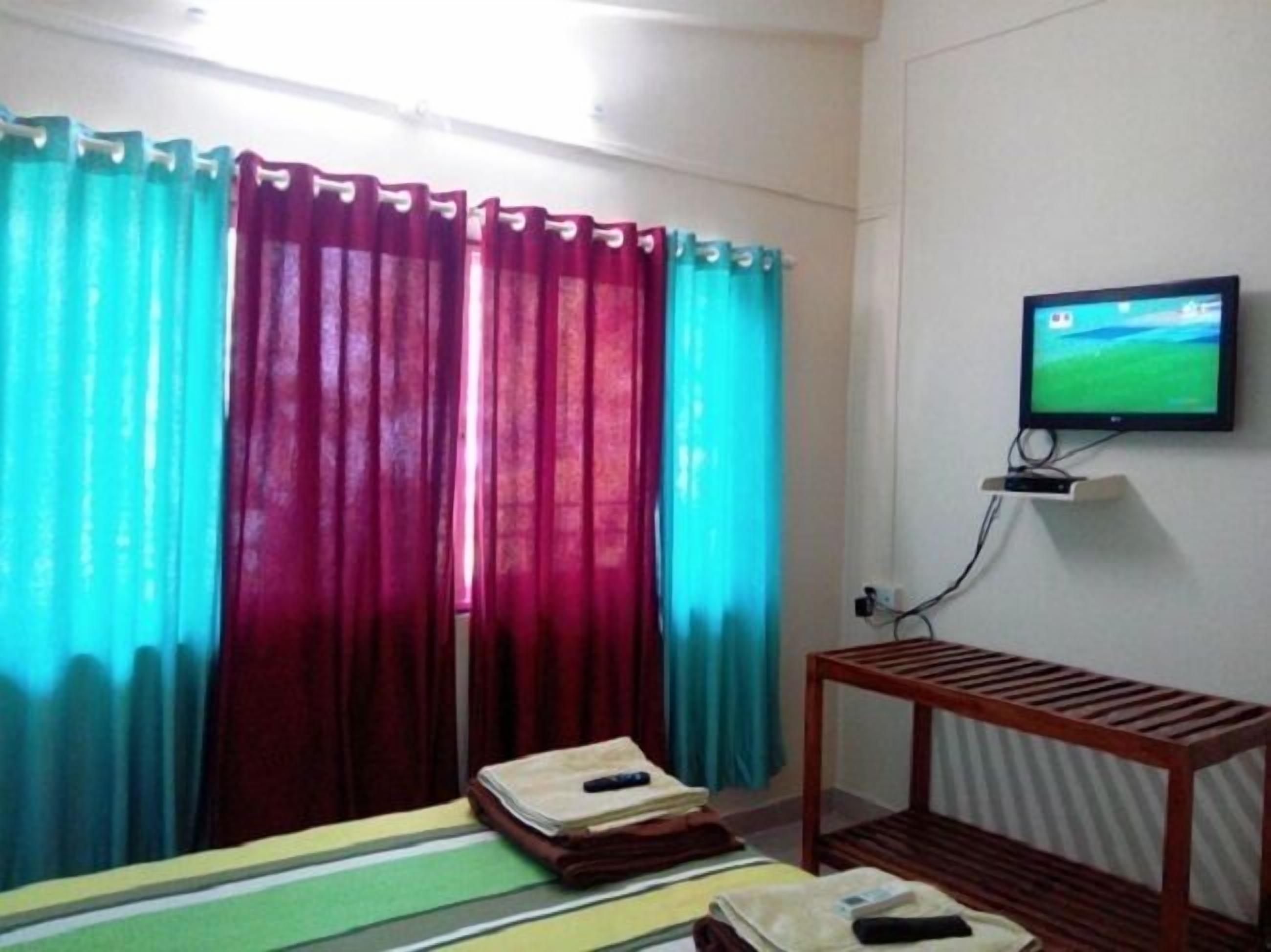 A hotel room with a bed, a TV mounted on the wall, and curtains.