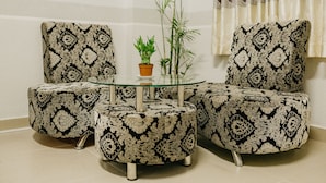 A corner seating area with a glass-top coffee table, two patterned armchairs, and a small potted plant. - Levit'ss (Xuan Huong - Da Lat)