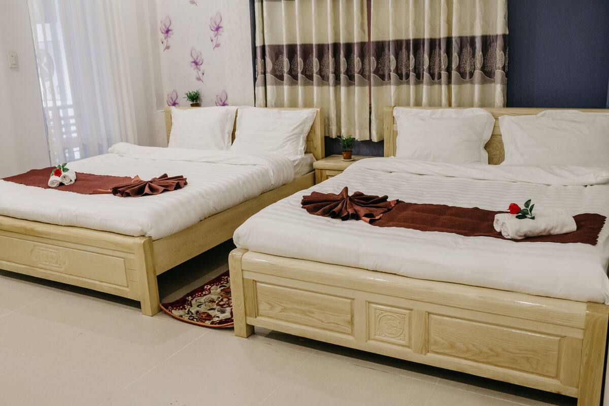 Two twin beds with white linens, brown throw blankets, and a small potted plant on a nightstand.