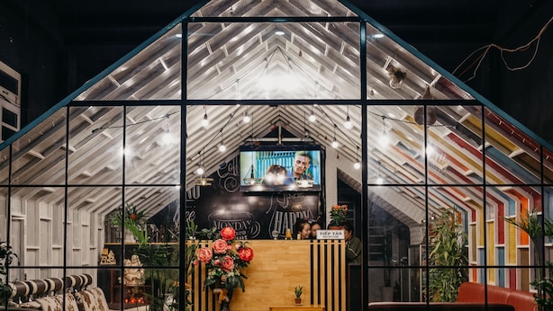 A reception area with a modern design, featuring a wooden reception desk, a television screen, and a staircase leading to upper levels. - Levit'ss (Xuan Huong - Da Lat)
